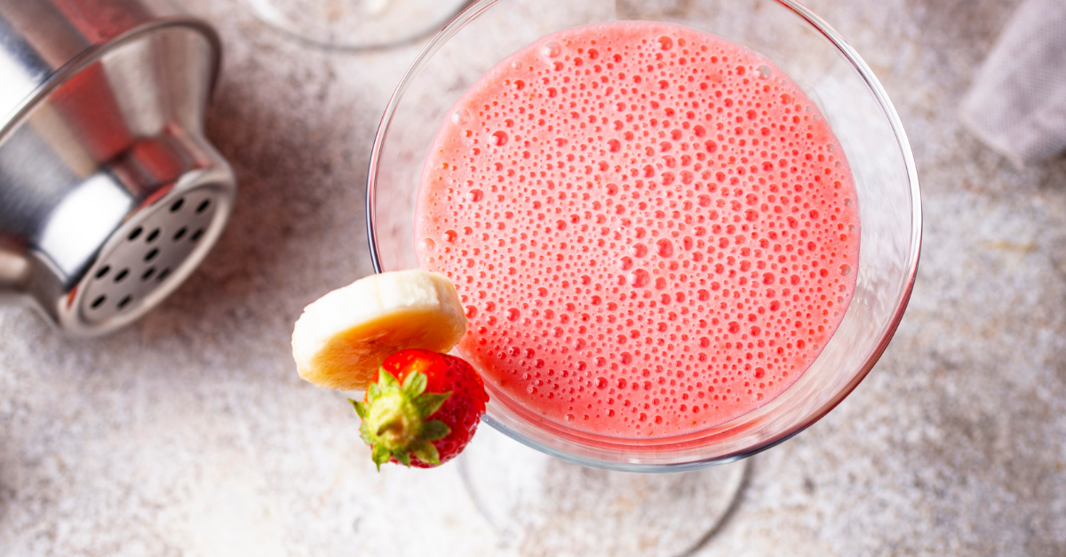 strawberries and cream cocktail in a martini glass garnished with fresh banana slice and a strawberry