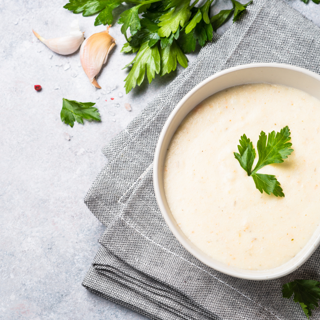 Big white bowl of chicken soup garnished with fresh parsley. On a neatly folded grey tea towel