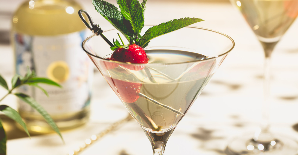 Classic martini cocktail in a beautiful martini glass garnished with a strawberry and some fresh mint leaves on a cocktail pick