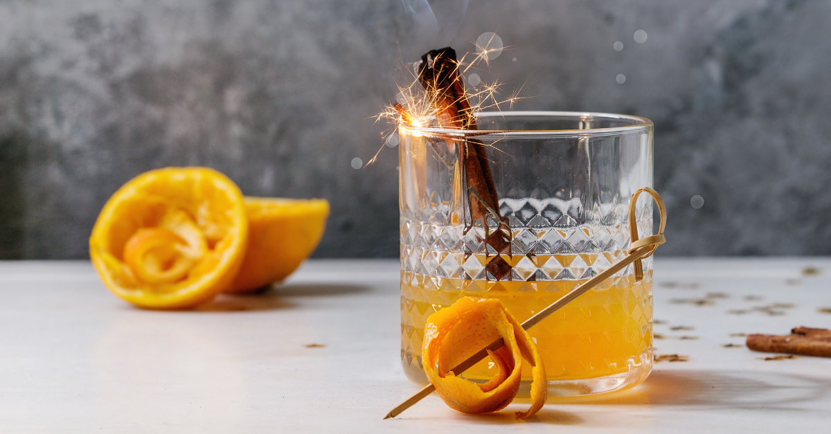 Smokey tea sours with rolled orange peel garnish and a small sparkler in the cut glass tumbler