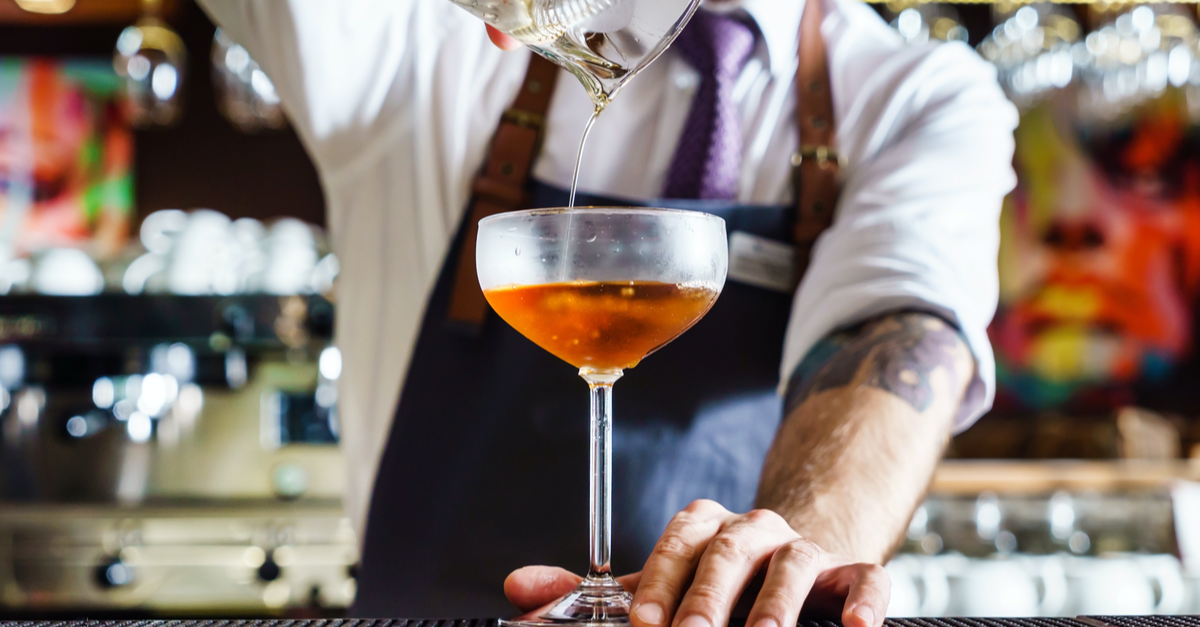 bartender pouring a cockail in a coupe glass from a height